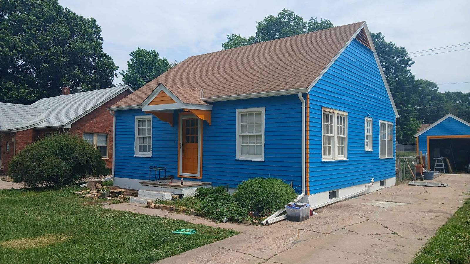 A small gabled house painted bright cobalt blue, with white-trimmed windows and an orange front door.