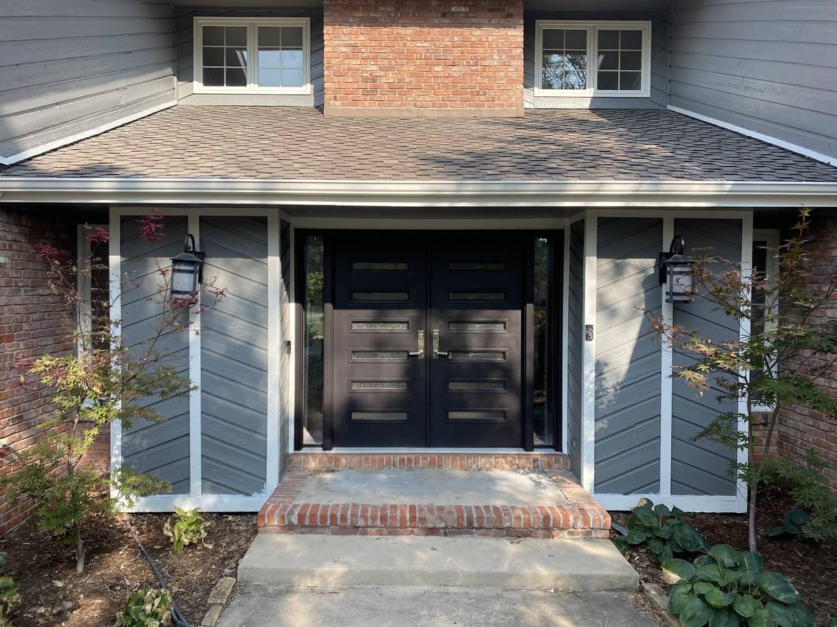 A double front door painted black, set in white trim between gray siding panels above a brick step.