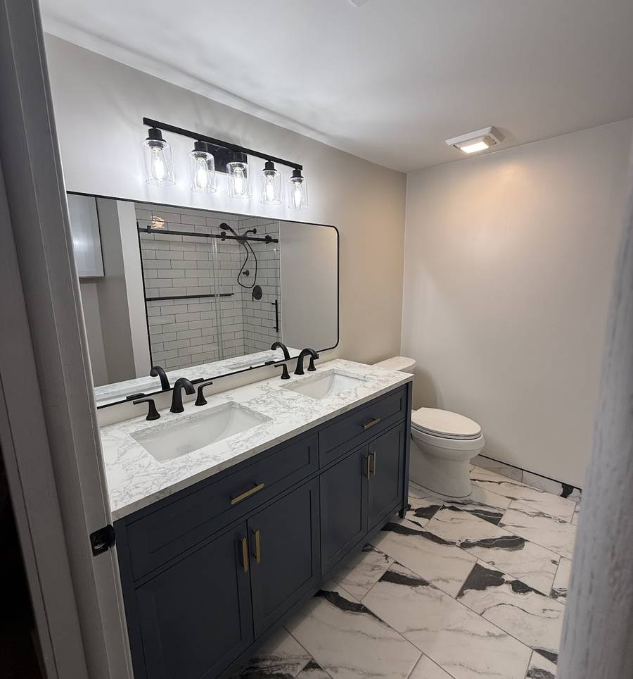 A bathroom with a navy double vanity, white top, black faucets and black-and-white marble-look floor tile.